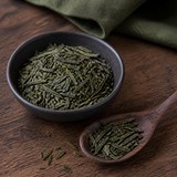 Organic Sencha green tea leaves in a dark ceramic bowl and wooden spoon